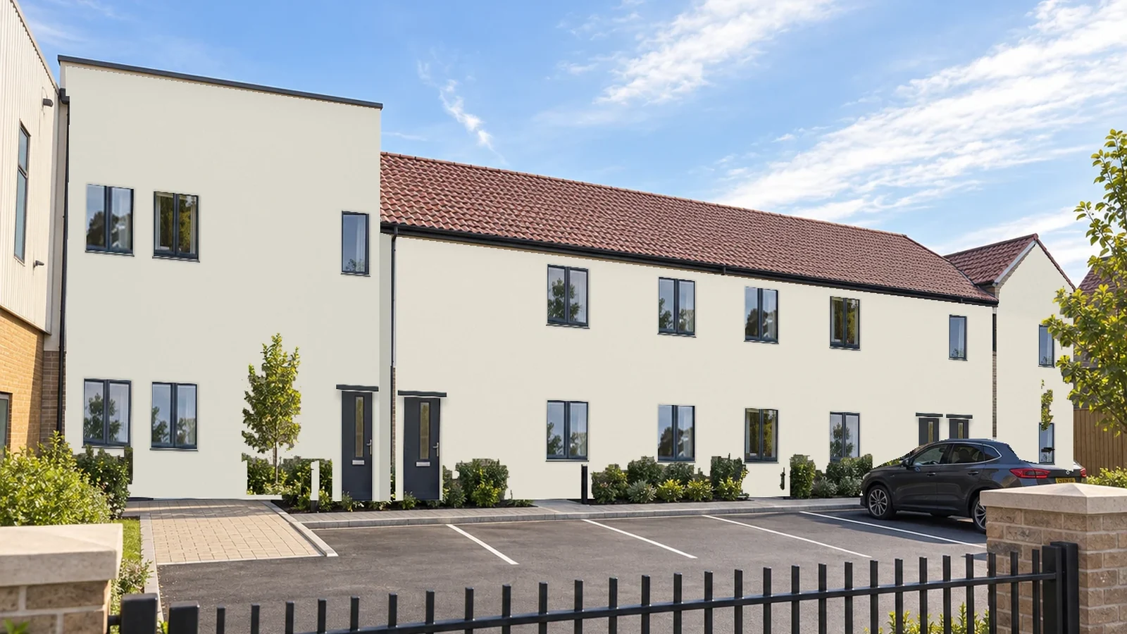 Rendered view of the converted two-storey building in white render with grey windows and doors, a flat-roofed block at one end and a pitched clay-tiled roof beyond, seen across the new car park and railings