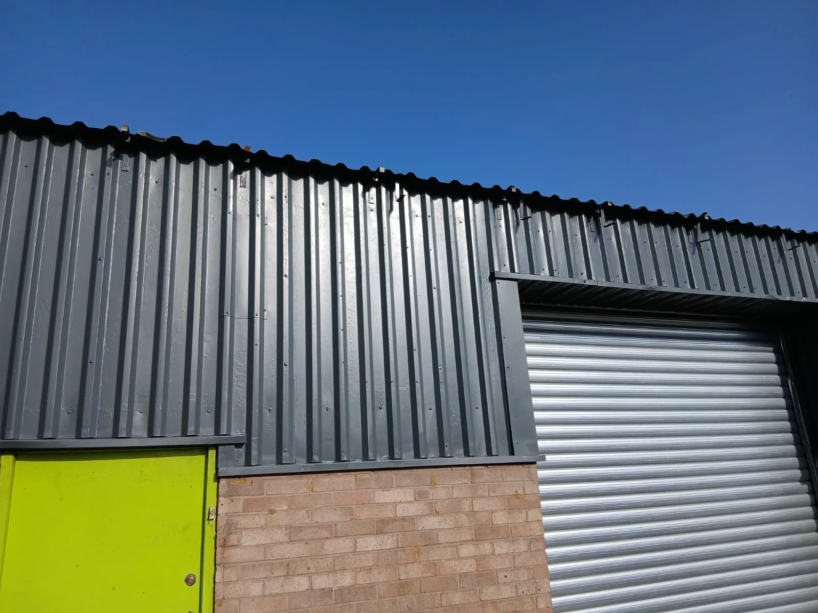 Industrial unit with repaired dark grey cladding, new roller shutter and lime green personnel door