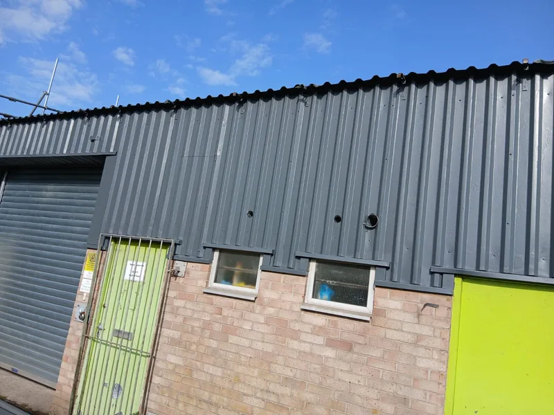 Corner of an industrial unit showing repaired cladding above brickwork