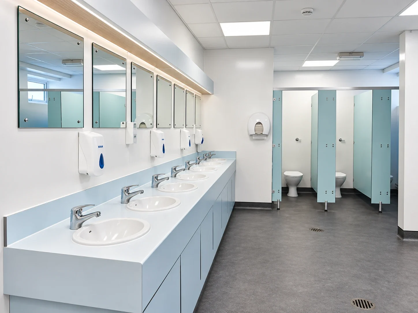 Refurbished washroom with white vanity units, mirrors and new cubicles