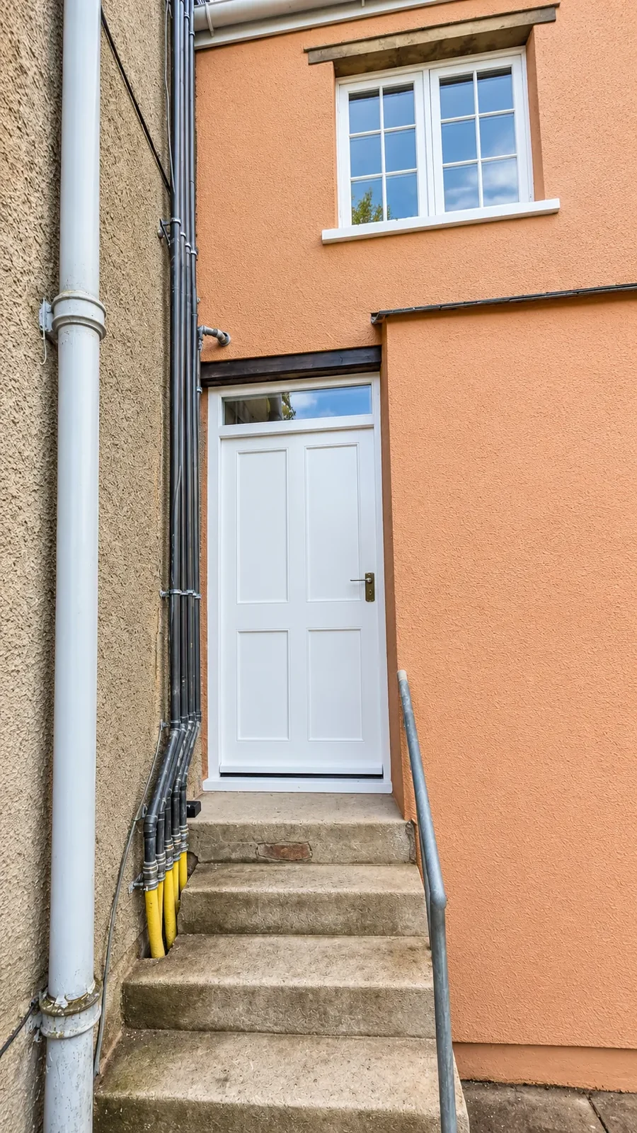 Rendered east wing of the country house with new cast-iron rainwater goods and a painted door